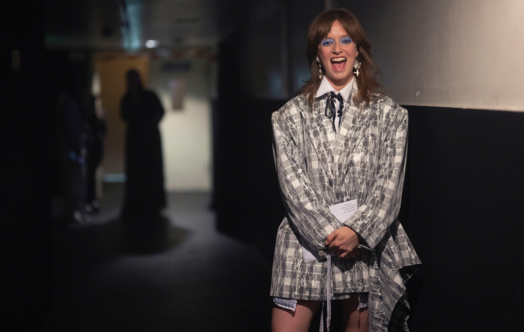 Orla Gartland wearing grey, standing in darkened corridor at The Ivor Novello Awards 2025.