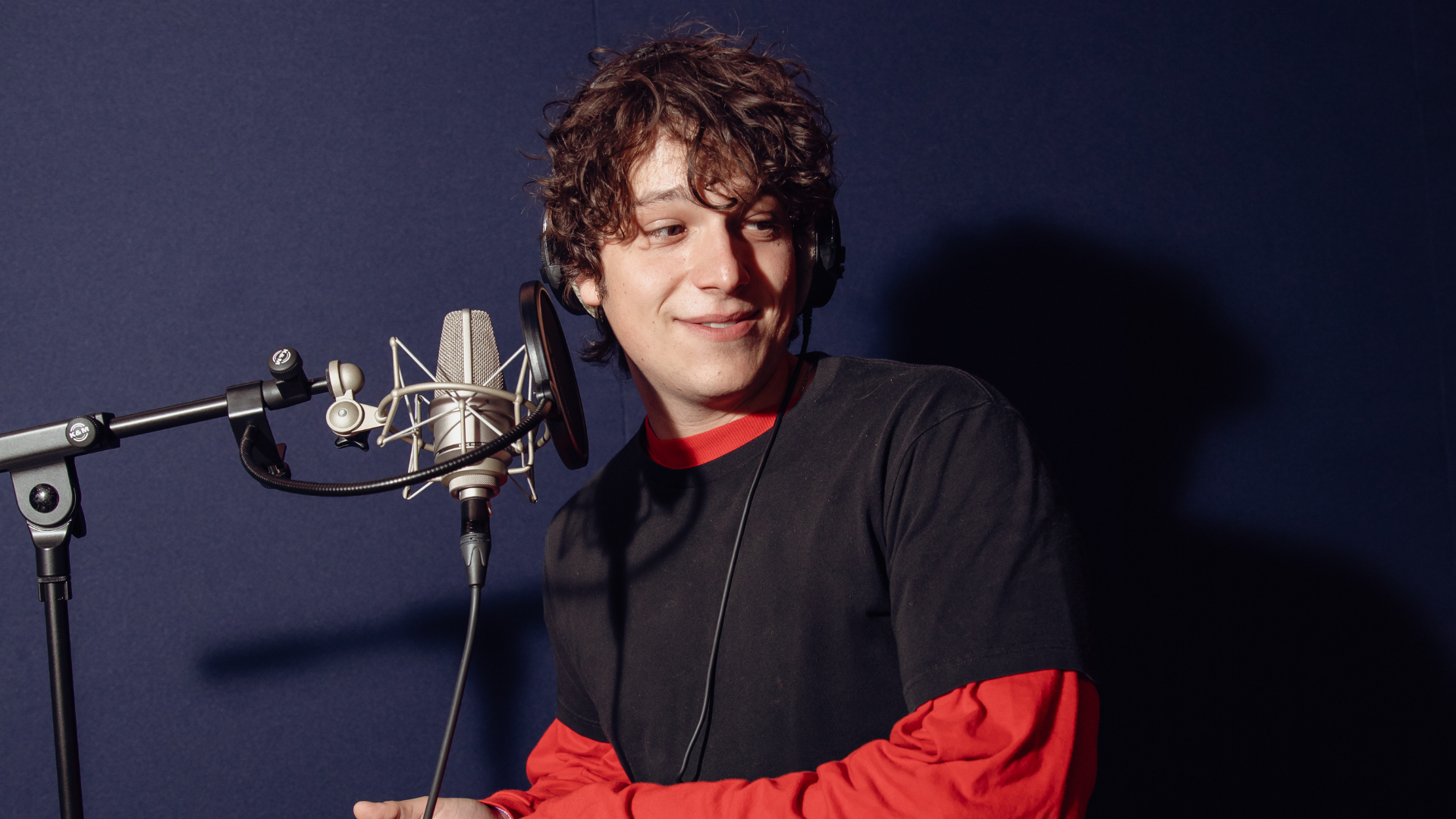 Man in blue and red top smiling in front of a mic in a studio